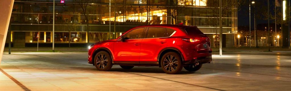 Red Mazda CX-5 parked in a lit city plaza at night.