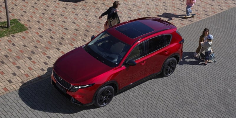 Red Mazda CX-5 SUV parked on a paved plaza with pedestrians nearby.